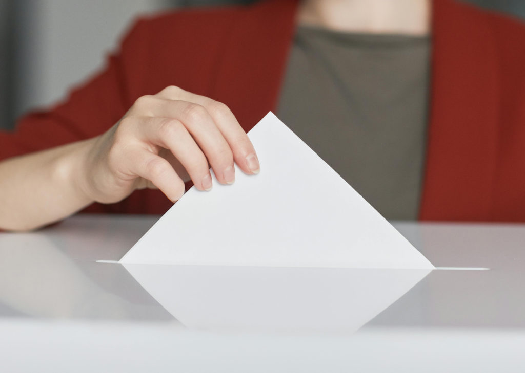A woman posts a voting ballot into a ballot box.
