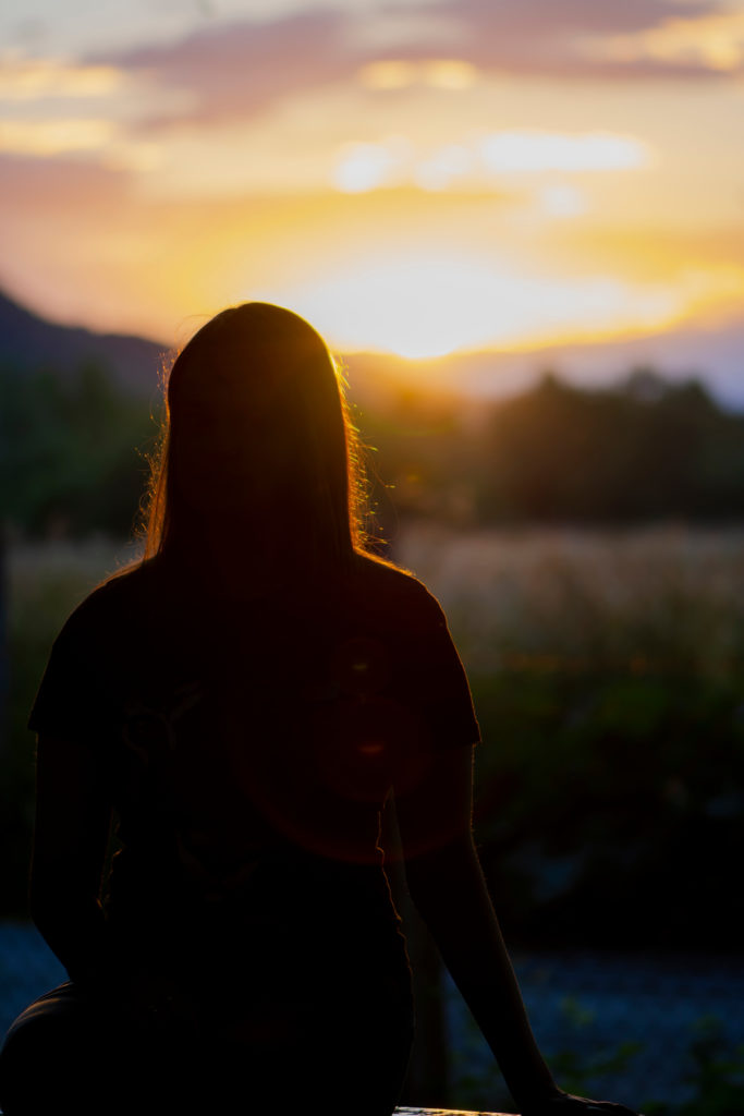 A photo of a young woman with her back to us as a sign rises in the distance, making the young woman appear like a silhouette.