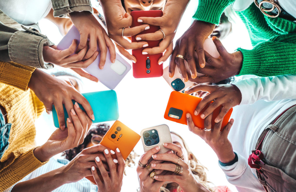 A photo of young people standing in a circle on their mobile phones. The photo is taken from inside the circle looking up.