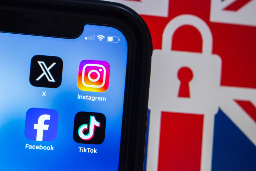 An image of the top right corner of a mobile phone with social media app icons on the screen and a Union Jack flag behind it with a lock in its middle.