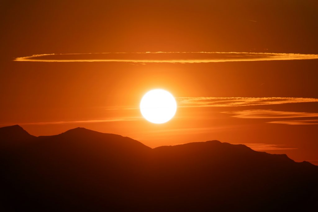A photo of the sun in an orange sky with silhouettes of hills.